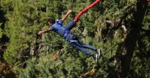A man experiences the thrill of bungee jumping over a forest, showcasing adventure and excitement.