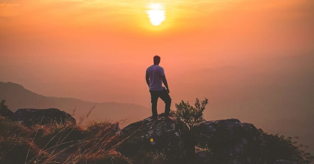 A lone hiker admires a stunning sunset view from Ponmudi Peak, creating a serene landscape scene.
