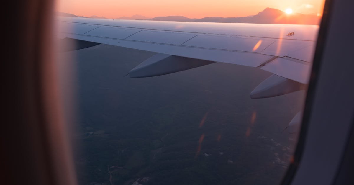 Airplane wing view through window during sunset, capturing a serene sky and landscape below.